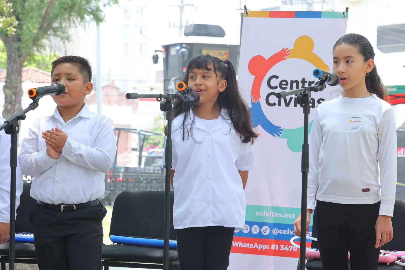 Niñas y niños del Coro Cívitas cantando frente a micrófonos en la Alameda de Pinta